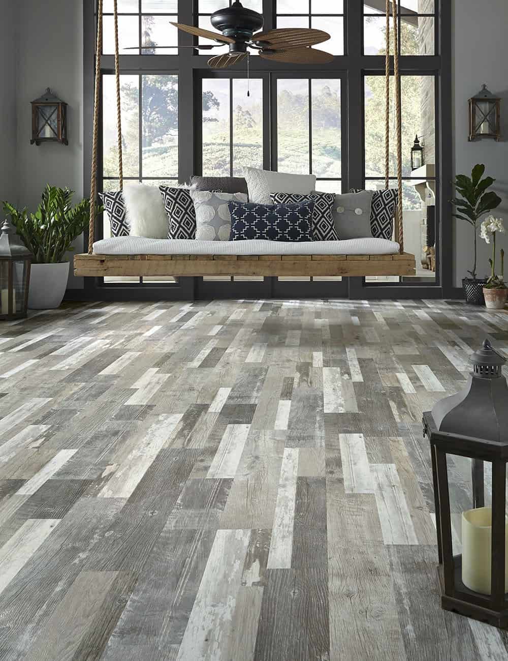 Weathered gray luxury vinyl plank floor in a sunroom with a hanging bench swing